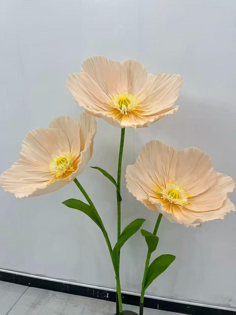 Peut inclure: Trois grandes fleurs artificielles avec des p&eacute;tales couleur p&ecirc;che et des centres jaunes. Les fleurs ont des tiges et des feuilles vertes. Les p&eacute;tales ont un aspect textur&eacute;. Les fleurs sont probablement &agrave; des fins d&eacute;coratives.