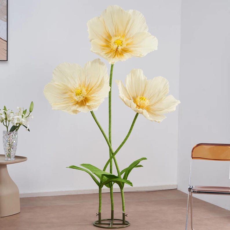 Peut inclure: Composition florale d&eacute;corative avec trois grandes fleurs de pavot artificielles cr&egrave;me, centres jaunes et tiges vertes. Les fleurs sont dispos&eacute;es dans un support m&eacute;tallique avec des feuilles vertes. D&eacute;coration int&eacute;rieure moderne.