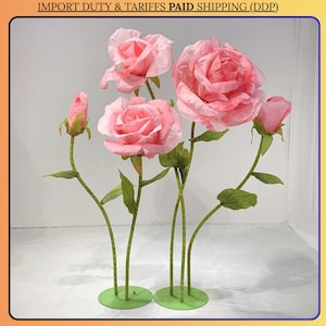 May include: A cluster of large, pink paper roses with green stems and leaves. The roses are in various stages of bloom, from buds to fully open flowers. The stems are attached to green circular bases.