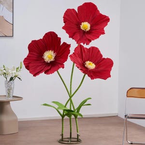 Peut inclure: Une composition florale d&eacute;corative avec trois grandes fleurs de pavot rouge vif et des centres jaunes. Les fleurs ont des tiges et des feuilles vertes, et sont fix&eacute;es dans une base m&eacute;tallique circulaire. Un &eacute;l&eacute;ment de d&eacute;coration int&eacute;rieure saisissant.