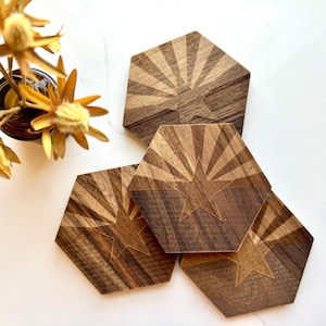 May include: Four hexagonal wooden coasters with a star and sunburst design. The coasters are made of dark wood with a light brown wood inlay.