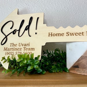 May include: A wooden key-shaped sign with the words "Sold!" and "Home Sweet Home!"  The sign also includes the text "The Uvari Martinez Team (602) 578-5600".