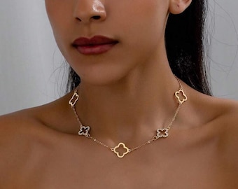 May include: A gold-colored necklace featuring clover-shaped pendants. Some of the pendants are adorned with small, sparkling crystals. The necklace is delicate and appears to be made of a thin chain.