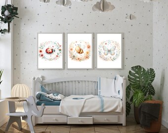 May include: Three framed prints with watercolor illustrations of a ladybug, a bee, and a butterfly. Each illustration is surrounded by a wreath of flowers. The prints are hanging on a white wall with a gray star pattern.
