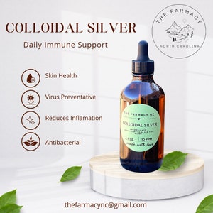 May include: A brown glass bottle with a dropper top, labeled "The Farmacy NC Colloidal Silver 4 oz 10 PPM made with love". The bottle is sitting on a wooden surface with green leaves. The label also includes the text "Ingredients: Purified Water & 10 PPM Pure Silver".