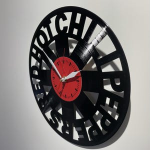 May include: A black vinyl record clock with the words "HOTCHILIPEPPERS" cut out around the edge. The clock face is red with white hands.