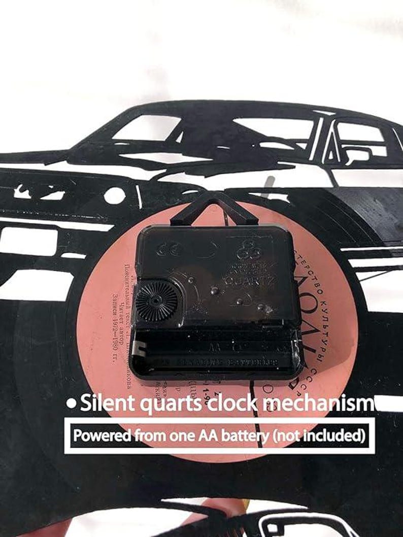 May include: A black vinyl record clock featuring a silhouette of a car. The clock mechanism is visible on the back of the record. The text "Silent quarts clock mechanism" and "Powered from one AA battery (not included)" is printed below the record.
