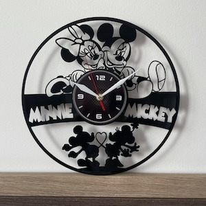 Könnte beinhalten: Schwarz-weiße Vinyl-Plattenuhr mit Mickey Mouse und Minnie Mouse. Das Zifferblatt der Uhr ist schwarz mit weißen Zahlen und Zeigern. Die Wörter "Minnie" und "Mickey" sind auf der Schallplatte geschrieben.