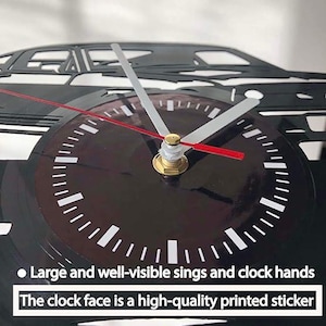 May include: Black and white vinyl record clock with a silhouette of a car. The clock face has a black background with white markings and large, easy-to-read clock hands. The text "Large and well-visible sings and clock hands" and "The clock face is a high-quality printed sticker" is visible below the clock face.