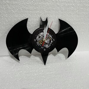 K&ouml;nnte beinhalten: Schwarze Schallplattenuhr in Form des Batman-Logos. Das Zifferblatt hat ein sichtbares Getriebe und r&ouml;mische Ziffern.