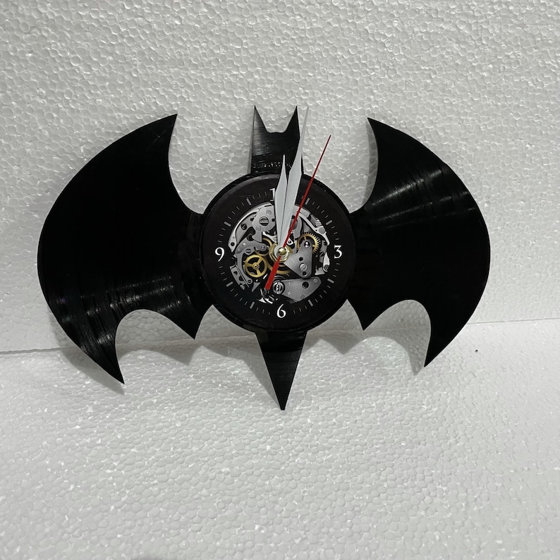 K&ouml;nnte beinhalten: Schwarze Schallplattenuhr in Form des Batman-Logos. Das Zifferblatt hat ein sichtbares Getriebe und r&ouml;mische Ziffern.