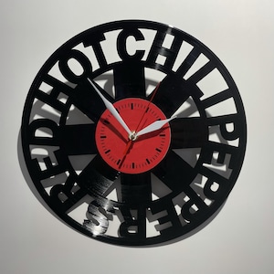 May include: A black vinyl record clock with the words "Red Hot Chili Peppers" cut out around the edge. The clock face is red with white hands.