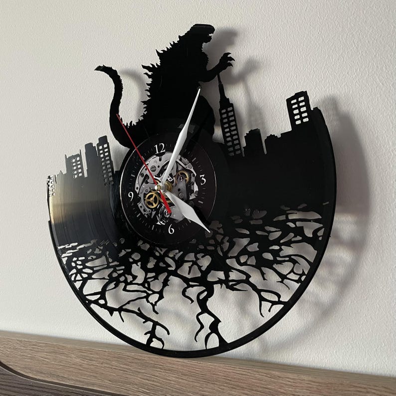 May include: Black vinyl record clock featuring a silhouette of Godzilla destroying a city skyline. The clock face is visible with Roman numeral markings and a white hand.
