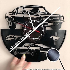 May include: A black vinyl record clock featuring a silhouette of a Ford Mustang GT. The clock is 12 inches in diameter and is made from a real vinyl record in good condition. "The size is 12 inches in diameter" and "The clock is made from a real vinyl record in good condition" are written below the clock.