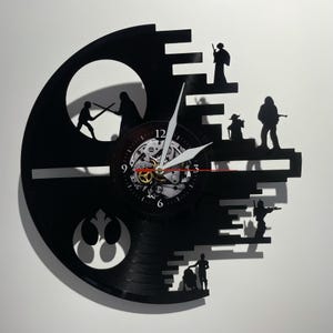Könnte beinhalten: Eine schwarze Schallplattenuhr mit einer Silhouette des Todessterns aus Star Wars. Das Zifferblatt der Uhr ist ein kleinerer Kreis mit römischen Ziffern und einem weißen und roten Zeiger. Die Silhouette des Todessterns besteht aus schwarzen Balken und enthält Silhouetten von Star Wars-Charakteren.