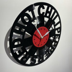 May include: Black vinyl record clock with the words "Red Hot Chili Peppers" cut out around the edge. The clock face is red with black numbers and hands.