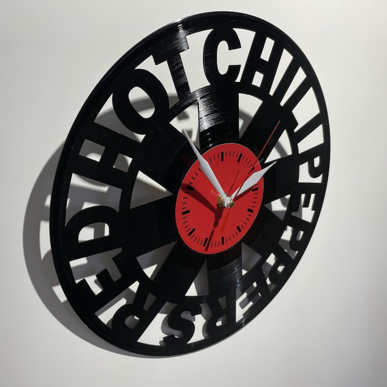 May include: Black vinyl record clock with the words "Red Hot Chili Peppers" cut out around the edge. The clock face is red with black numbers and hands.
