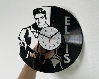May include: Black and white vinyl record clock featuring a silhouette of Elvis Presley. The clock face is white with black numbers and hands. The record is labeled "Elvis" in a stylized font.