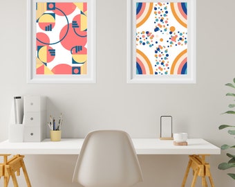 May include: Two framed abstract art prints with geometric shapes and patterns in shades of pink, yellow, blue, and white. The prints are hanging on a white wall above a white desk with a white chair.