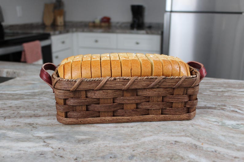 Puede incluir: Una cesta de pan de mimbre marr&oacute;n con asas de cuero rojo, llena de rebanadas de pan blanco.