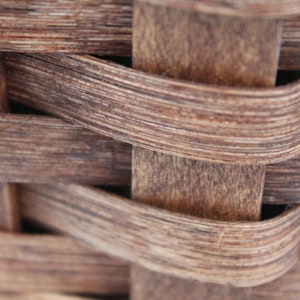 K&ouml;nnte beinhalten: Nahaufnahme eines geflochtenen Korbes aus braunem Holz. Der Korb besteht aus d&uuml;nnen Holzstreifen, die miteinander verflochten sind, um ein dichtes, stabiles Geflecht zu bilden.