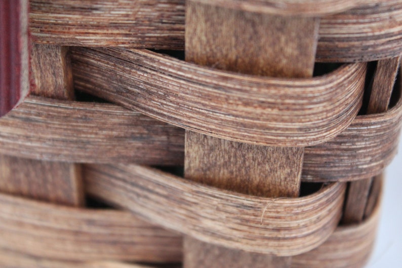 K&ouml;nnte beinhalten: Nahaufnahme eines geflochtenen Korbes aus braunem Holz. Der Korb besteht aus d&uuml;nnen Holzstreifen, die miteinander verflochten sind, um ein dichtes, stabiles Geflecht zu bilden.