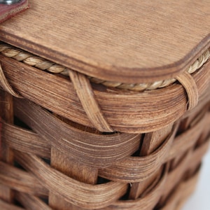 K&ouml;nnte beinhalten: Ein brauner Weidenkorb mit einem Holzdeckel und einem braunen Lederriemen mit einem Metallknopf. Der Korb hat ein geflochtenes Design und ist aus nat&uuml;rlichen Materialien gefertigt.