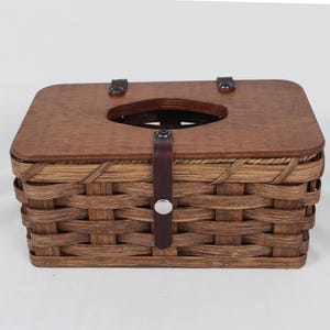 K&ouml;nnte beinhalten: Ein brauner geflochtener Tissuebox-Bezug mit einem Holzdeckel und einem Lederriemen mit einer Metallschnalle.