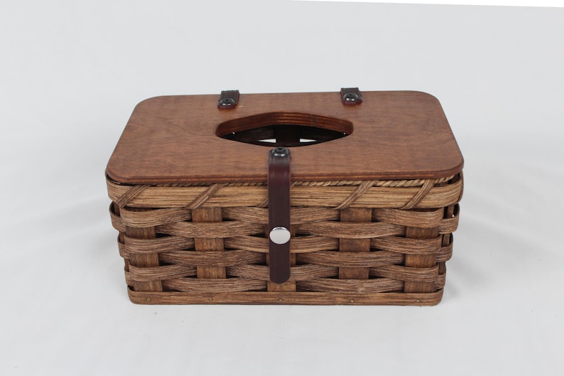 K&ouml;nnte beinhalten: Ein brauner geflochtener Tissuebox-Bezug mit einem Holzdeckel und einem Lederriemen mit einer Metallschnalle.