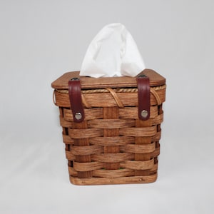 K&ouml;nnte beinhalten: Ein geflochtener Holz-Tischdeckenhalter mit braunen Lederriemen und Metallschnallen. Der Halter ist mit wei&szlig;en Taschent&uuml;chern gef&uuml;llt.