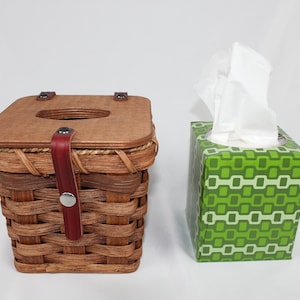 K&ouml;nnte beinhalten: Zwei Taschentuchboxen. Eine ist ein geflochtener Weidenkorb mit einem Holzdeckel und einem Lederriemen. Die andere ist eine Schachtel aus Pappe mit einem gr&uuml;n-wei&szlig;en geometrischen Muster.