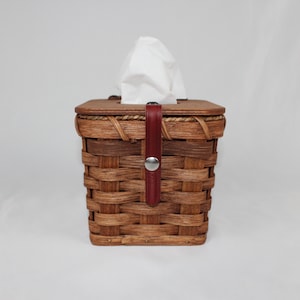 May include: A woven wicker tissue box cover with a red leather strap and a silver button closure.