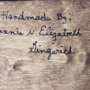 K&ouml;nnte beinhalten: Handgefertigt von: Bernie & Elizabeth Gingerich. Dies ist eine handschriftliche Notiz auf einer Holzoberfl&auml;che.
