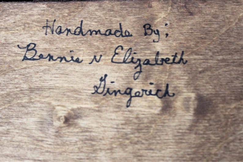K&ouml;nnte beinhalten: Handgefertigt von: Bernie & Elizabeth Gingerich. Dies ist eine handschriftliche Notiz auf einer Holzoberfl&auml;che.