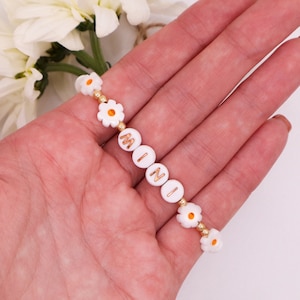 May include: White daisy charm bracelet with gold beads and the name "MINI" spelled out in gold letters.