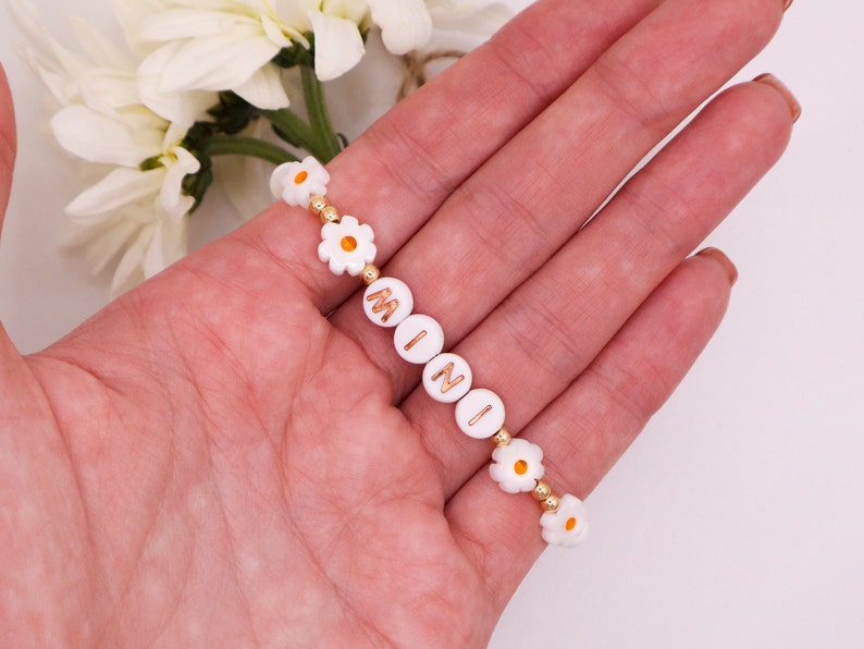 May include: White daisy charm bracelet with gold beads and the name "MINI" spelled out in gold letters.