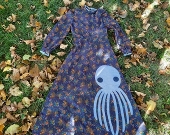 May include: A long-sleeved dress featuring a dark blue fabric with a dense floral pattern in orange, red, and green. A large, light blue and white gingham octopus appliqué with two dark circular buttons for eyes is positioned on the skirt.