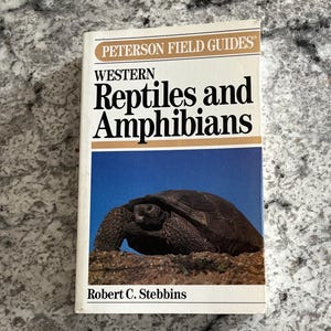 May include: A paperback field guide titled Peterson Field Guides Western Reptiles and Amphibians by Robert C. Stebbins. The white cover features a photograph of a dark-coloured tortoise on brown earth against a bright blue sky background.