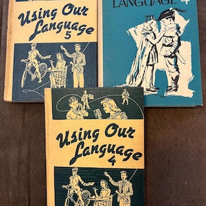May include: Three vintage textbooks titled "Using Our Language" are displayed. The books have blue and cream covers with illustrations of children and text. The covers feature illustrations of children, microphones, and figures on bicycles.