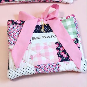 Könnte beinhalten: Zwei gesteppte Stoffbeutel mit einem Patchwork-Design in rosa, weißen und marineblauen Blumen- und Polka-Dot-Mustern. Jeder Beutel hat eine rosa Schleife und den Text "Bless Your Heart".