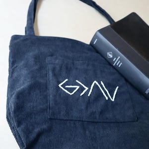 Unique handmade Christian corduroy tote bag embroidered with the phrase “God is Greater Than the Highs and Lows,” symbolizing strength and faith. Features a large outer pocket, zipper closure, and multi-pocket interior for organizing Bibles, journals, or personal items. Perfect for church, Bible study, or everyday wear. A meaningful Christian gift for women rooted in faith and perseverance. Back To School Book Bag For Girl faith-inspired god greater ups and downs.