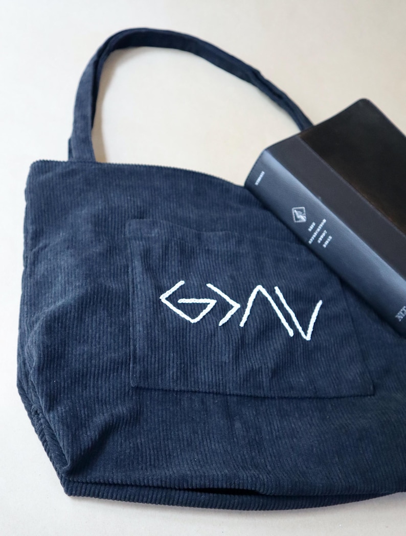 Unique handmade Christian corduroy tote bag embroidered with the phrase “God is Greater Than the Highs and Lows,” symbolizing strength and faith. Features a large outer pocket, zipper closure, and multi-pocket interior for organizing Bibles, journals, or personal items. Perfect for church, Bible study, or everyday wear. A meaningful Christian gift for women rooted in faith and perseverance. Back To School Book Bag For Girl faith-inspired god greater ups and downs.