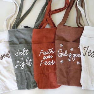 Hand embroidered corduroy tote bag with large pocket and zipper closure featuring Christian faith phrases like “God Is Good” and “Faith Over Fear.” Shown in warm neutral tones with roomy interior pockets — perfect for Bible study, church, school, or everyday use as a stylish Christian woman’s tote. Gift For Women Embroidered Corduroy Bible Tote Bag Faith Based Christian Gift Personalized Name Custom Church Bag Womens Fall Winter Book Tote Purse