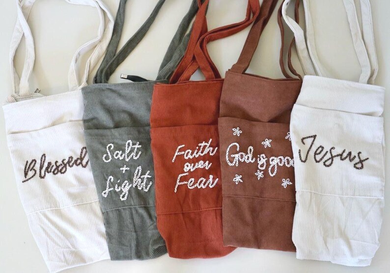 Hand embroidered corduroy tote bag with large pocket and zipper closure featuring Christian faith phrases like “God Is Good” and “Faith Over Fear.” Shown in warm neutral tones with roomy interior pockets — perfect for Bible study, church, school, or everyday use as a stylish Christian woman’s tote. Gift For Women Embroidered Corduroy Bible Tote Bag Faith Based Christian Gift Personalized Name Custom Church Bag Womens Fall Winter Book Tote Purse