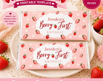 May include: Two rectangular candy wrappers with a light pink background featuring a repeating pattern of red strawberries and small white flowers. The center of each wrapper displays the text Jessica's Berry First Birthday. Dimensions are 7.4 by 6.5 inches.