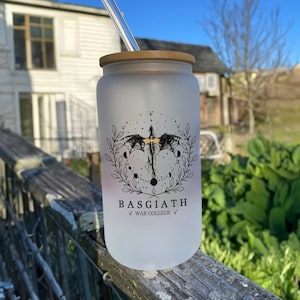 May include: A frosted glass water bottle with a bamboo lid and a black and gold design of a dragon with stars and moons. The bottle has the text "BASGIATH WAR COLLEGE" printed on it.