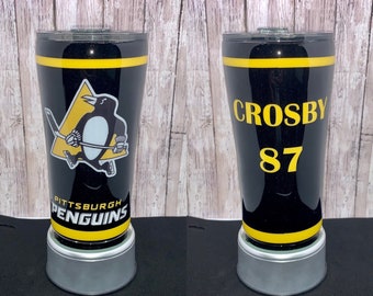 May include: Black and yellow tumbler with a Pittsburgh Penguins logo and the text "Pittsburgh Penguins" on one side and the text "Crosby 87" on the other side.