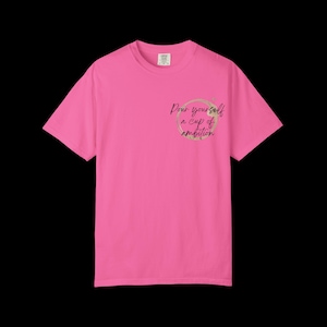 May include: A bright pink short-sleeve t-shirt featuring a circular coffee stain graphic on the left chest area. Inside the stain, the black cursive text reads, Pour yourself a cup of ambition. The shirt has a crew neckline and a standard fit.