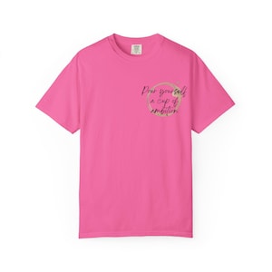 May include: A bright pink short-sleeve t-shirt featuring a circular coffee stain graphic on the left chest area. Inside the stain, the black cursive text reads, "Pour yourself a cup of ambition." The shirt has a crew neckline and a standard fit.
