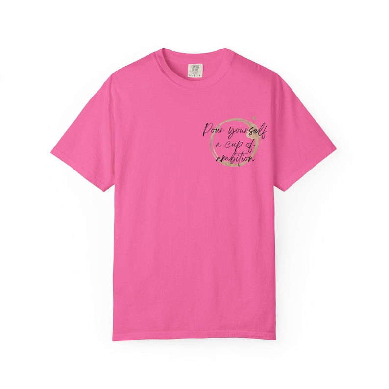 May include: A bright pink short-sleeve t-shirt featuring a circular coffee stain graphic on the left chest area. Inside the stain, the black cursive text reads, "Pour yourself a cup of ambition." The shirt has a crew neckline and a standard fit.
